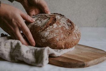 Immunsystem natürlich mit Sauerteig stärken:  Hände halten ein saftiges Krustenbrot auf einem Holzbrett