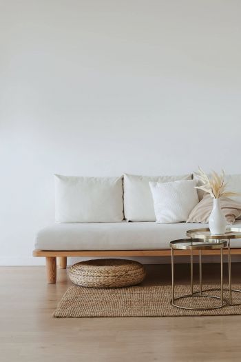 Mehr Ruhe im Alltag: Ausmisten. Zu sehen ist ein Wohnzimmerausschnitt in minimalistischem Design. Weiße Couch, weiße Vase, goldener Tisch, Teppich aus Bast.