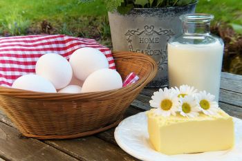 Immunsystem natürlich mit Vitamin A stärken: Auf einem Holztisch steht ein Korb mit Eiern, eine Karaffe mit Milch und ein Stück Butter auf einem Teller