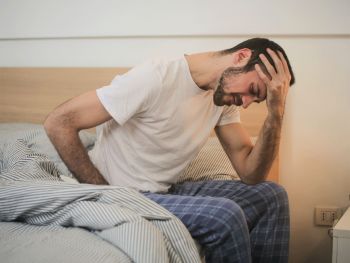 Symptome und Auswirkungen von stillen Entzündungen: zu sehen ist ein Mann im Schlafanzug, der auf der Bettkante sitzt und sich erschöpft den Kopf hält