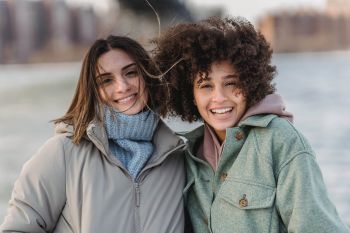 Mehr Ruhe im Alltag: Gesellschaft genießen. Zu sehen sind zwei junge Frauen, die sich im Arm halten und in die Kamera lächeln.